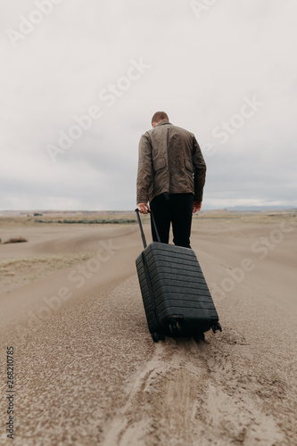 Man Walking Through Dunes Dragging Luggage photo
