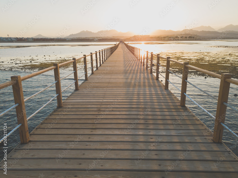 Beautiful view on sunset over the ocean, mountain and long wooden pier