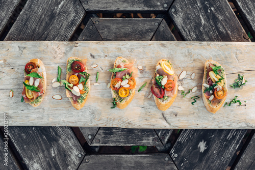 Overhead view of bruschetta topped with prosciutto and pesto served on table