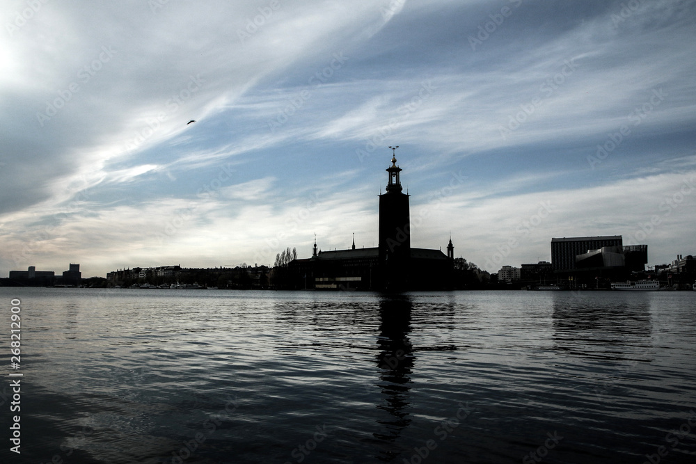 The silhouette of the town hall in Stockholm against the afternoon sun. The dark building is reflecting in the water.