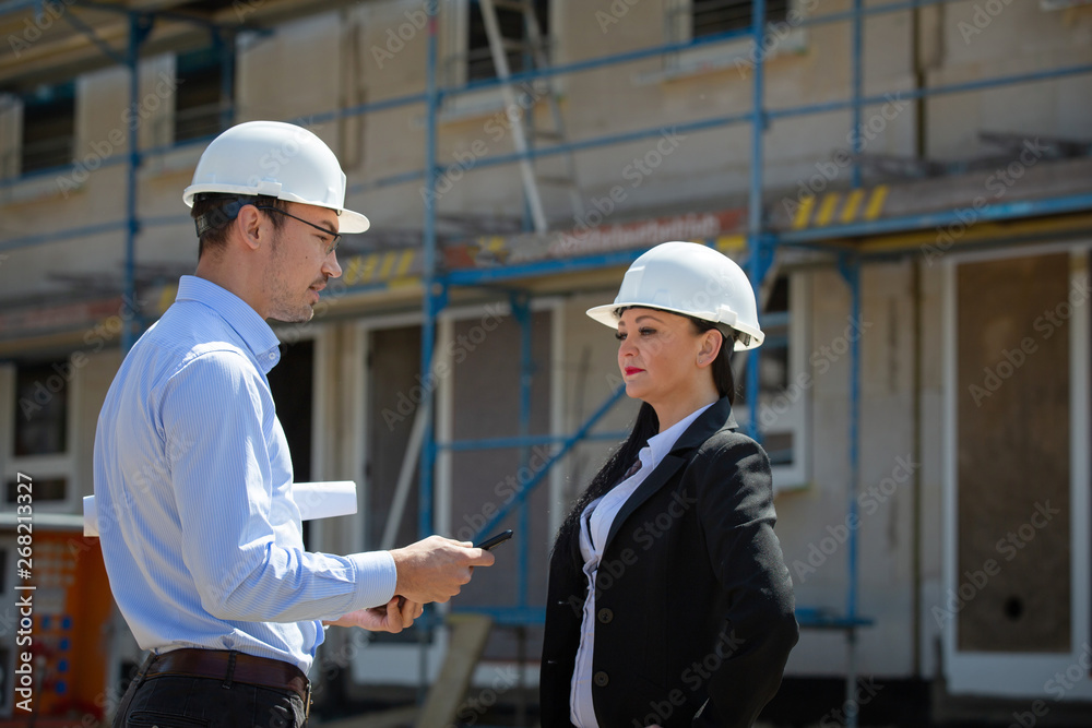 Two architects a man and a woman in construction in white helmets. Two architects a man and a woman in construction in white helmets.