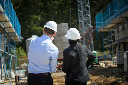 Two architects a man and a woman in construction in white helmets.