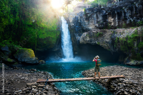 Travel photographer with backpack and camera in hand make epic photo amazing waterfall in the sun rays on background nature landscape