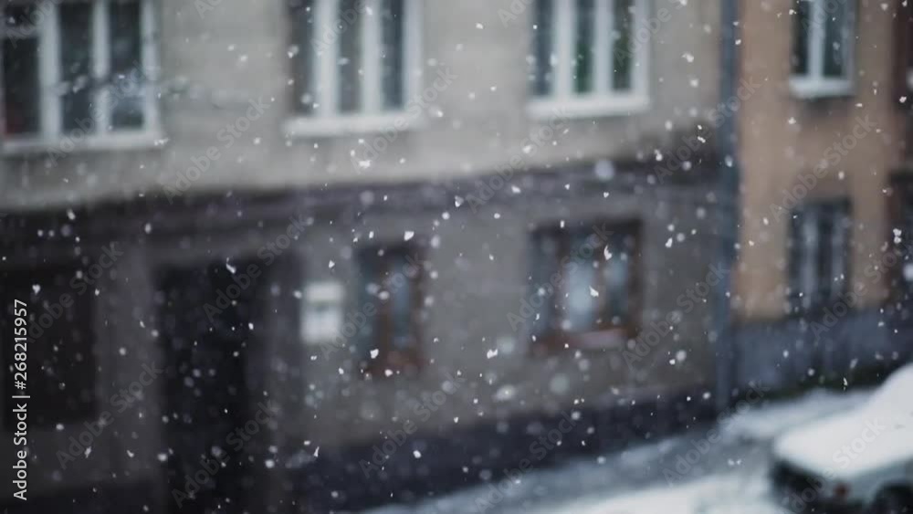 Beautiful slow-motion snowing in the city. View from the window of lovely snowfall against residential building.