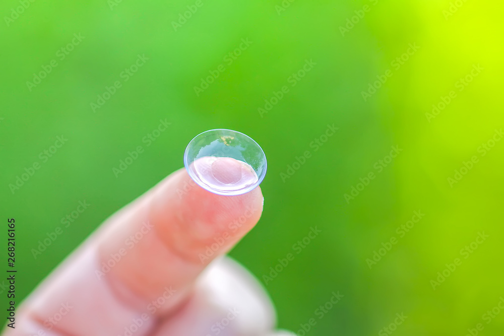 Transparent contact lens on finger tip on blurred green summer nature background Transparent contact lens on finger tip on blurred green summer nature background