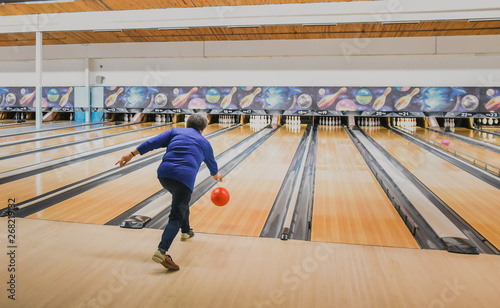 Older woman throwing bowling ball down a bowling lane.
