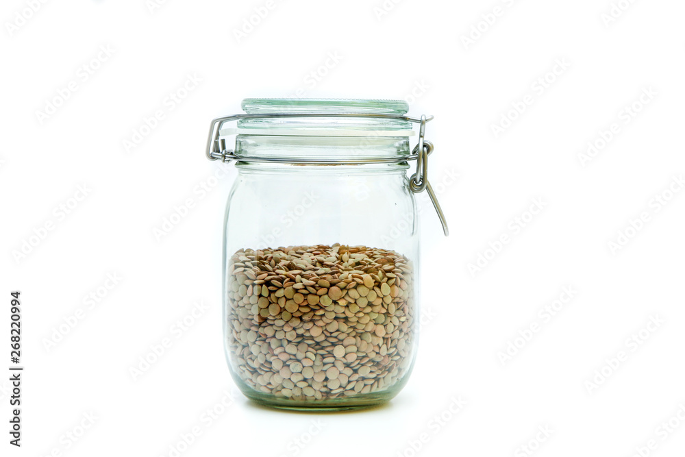 The green lentils stored inside the closable glass bottle isolated on a white background. The green lentils stored inside the closable glass bottle isolated on a white background.