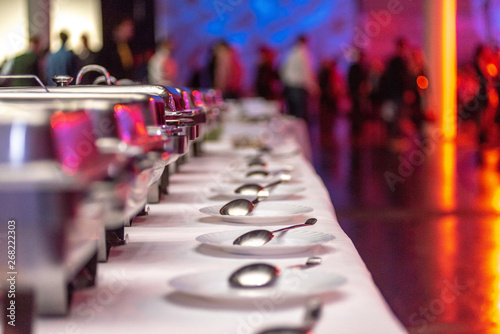 chafing-dishes mit tellern und besteck und menschen im hintergrund