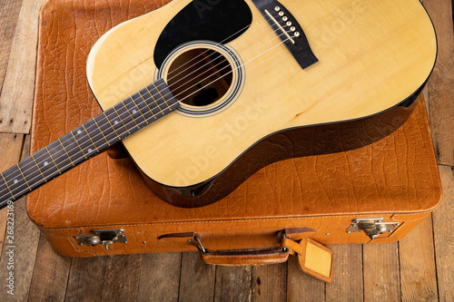 Classical guitar and suitcase on a dark wooden table. Stringed musical instrument on the go.