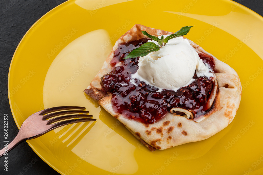 Pancakes or crepes with jam and ice cream decorated with mint on a plate over dark background. Breakfast food. Top view. Pancakes or crepes with jam and ice cream decorated with mint on a plate over dark background. Breakfast food. Top view.