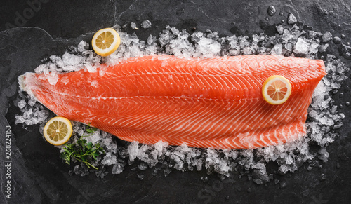 Fresh raw salmon fish steak with spices on ice over dark stone background. Creative layout made of fish, top view, flat lay. photo