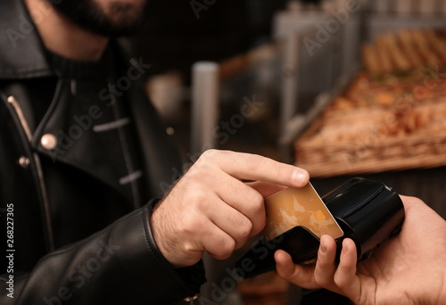 Man with credit card using payment terminal at shop, closeup