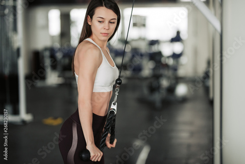 Athlete girl in sportswear working out and training her arms and shoulders with exercise machine in gym