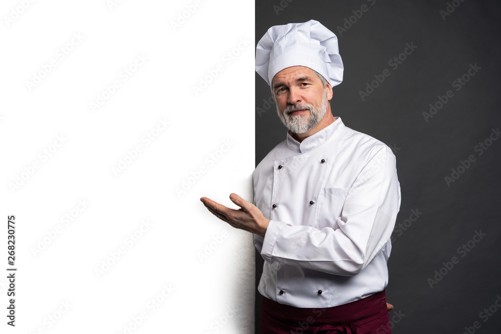 Portrait of a happy mature chef cook showing copyspace on the palms isolated on black background. - obrazy, fototapety, plakaty 