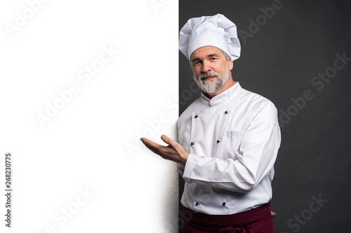 Portrait of a happy mature chef cook showing copyspace on the palms isolated on black background. photo