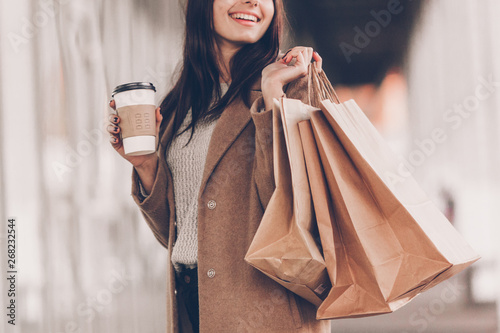 Beautiful fashionable woman with shopping bags and coffee walking near mall. photo
