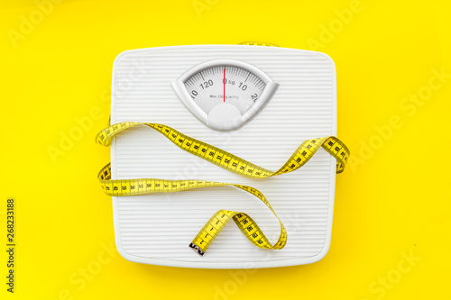 bathroom scales and measuring tape for weight loss concept on yellow background top view photo