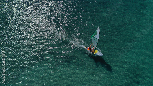 Aerial top view photo of fit man practising wind surfing in Mediterranean bay with crystal clear emerald sea