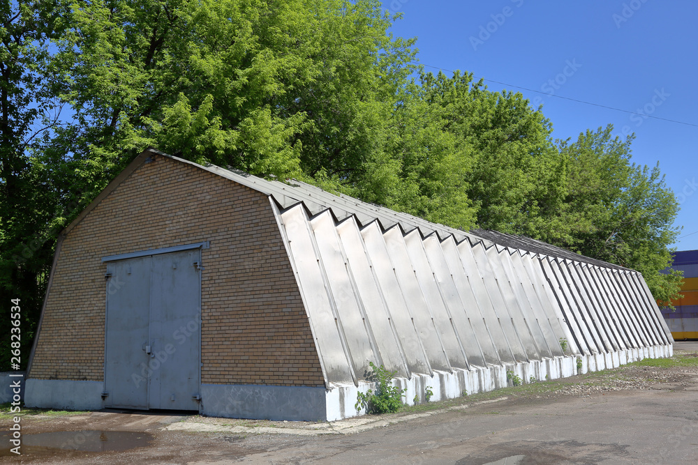 Obraz premium Industrial hangar with aluminum walls and roof stands on a concrete foundation near green trees