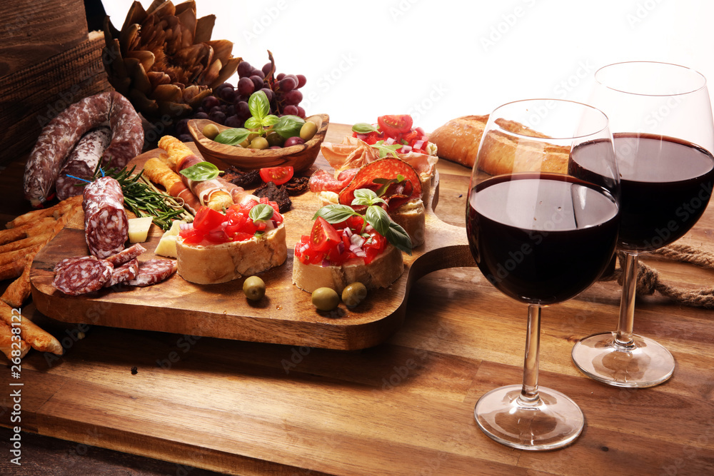 Traditional italian antipasto bruschetta appetizer with cherry tomatoes, cream cheese, basil leaves and balsamic vinegar on cutting board with prosciutto, salami, cheese