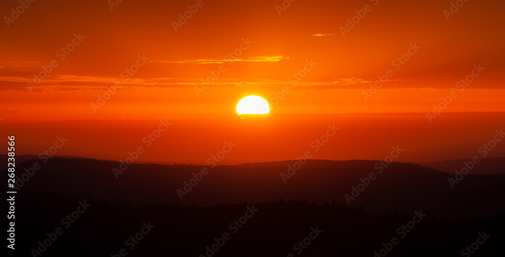 Scenic sunset over mountains. Glowing sun and orange sky and mountain range scenery or landscape.