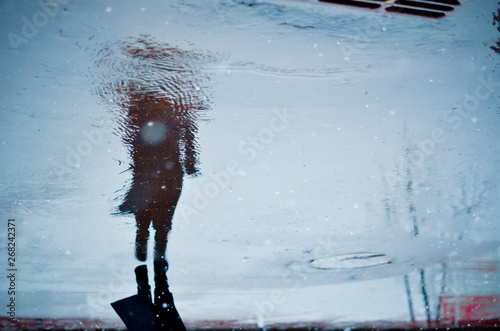 Blurry reflection in a puddle of alone walking person on wet city street during rain and snow. Mood concept photo
