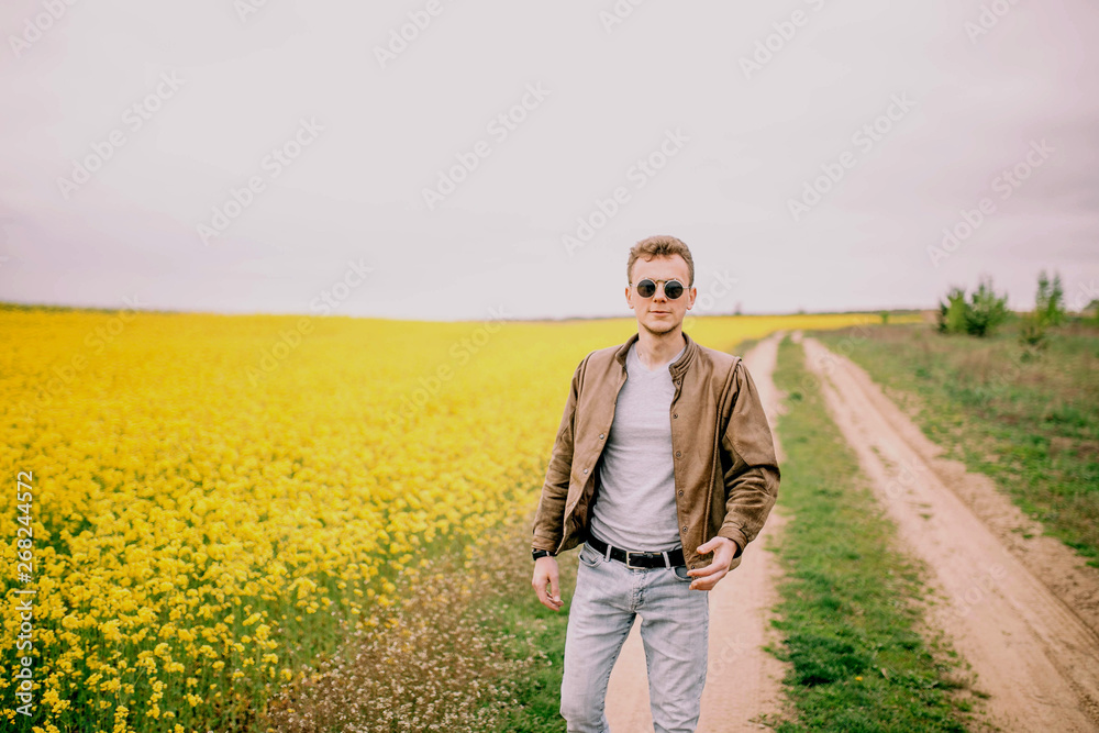 man wearing round steampunk sunglasses and a brown leather jacket in a summer yellow flowered field man wearing round steampunk sunglasses and a brown leather jacket in a summer yellow flowered field