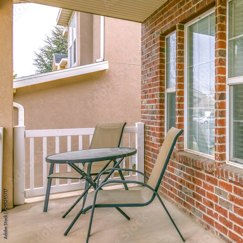 Clear Square Front porch of a home with table and chairs in front of brick wall and window