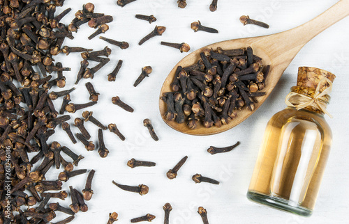 Fototapeta Naklejka Na Ścianę i Meble -  Close up glass bottle of clove oil and cloves in wooden spoon on white rustic table. Essential oil of clove rustic style background spice concept 