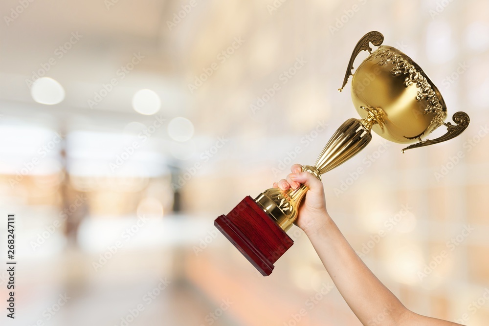Obraz premium Hand holding golden trophy on blurred background