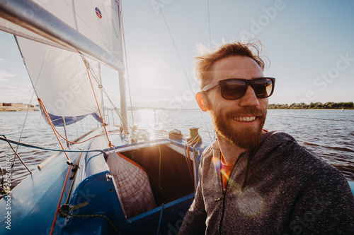 A handsome bearded man in sunglasses on a boat on a river or lake. Beautiful happy guy swimming in a boat on a autumn sunny day feeling free enjoying life