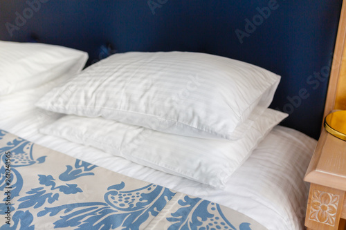 White pillows on the bed comfortable soft pillows on the bed in a stylish hotel room. Pillows lie on top of each other on a tucked-in bed with a blue headrest