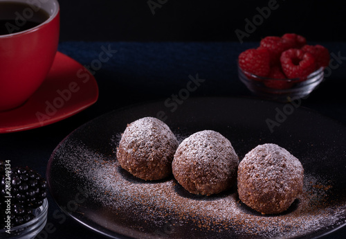 Homemade chocolate cake balls truffels sprinkled with powder sugar on black plate and red and black  raspberry with coffe cup   with dark background in rustic style. photo