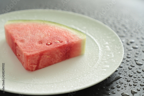 A slice of watermelon lies on a black background with water droplets