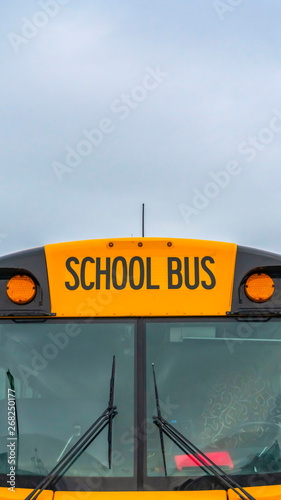 Vertical Front view of a yellow school bus with homes and cloudy sky in the background