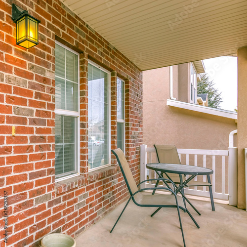 Square Front porch of a home with table and chairs in front of brick wall and window