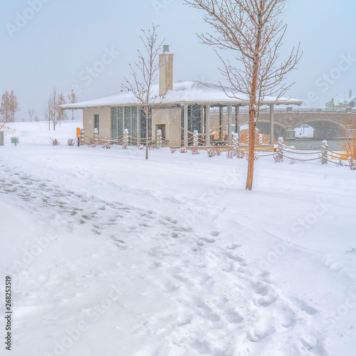 Square Snowy trail along Oquirrh Lake with view of a clubhouse and arched bridge