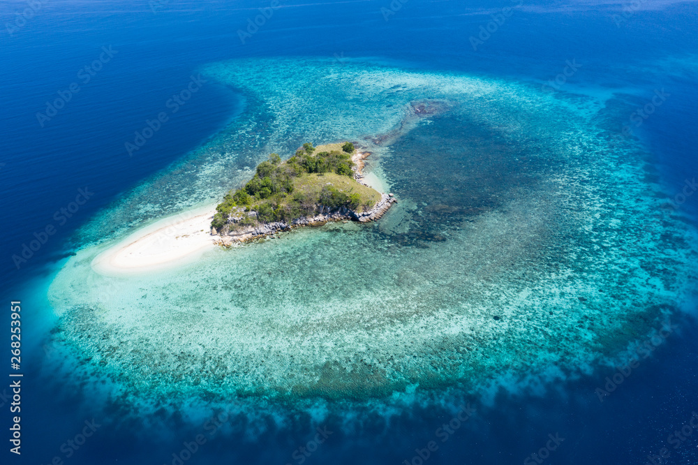 Seen from a bird's eye view, an idyllic island is surrounded by a healthy coral reef in Komodo National Park, Indonesia. This tropical area is known for its marine biodiversity as well as its dragons.