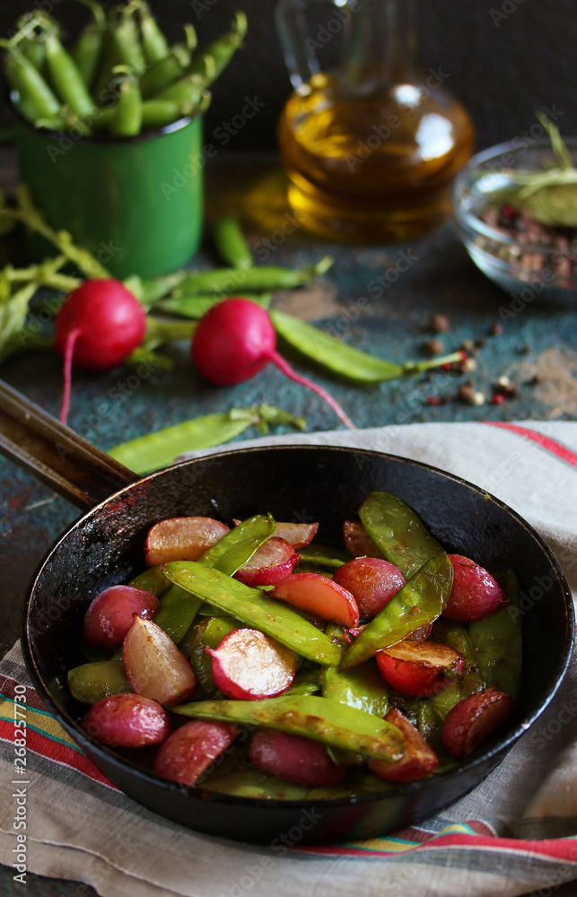 roasted young pods of peas and radish in a frying pan. light background. Soft focus