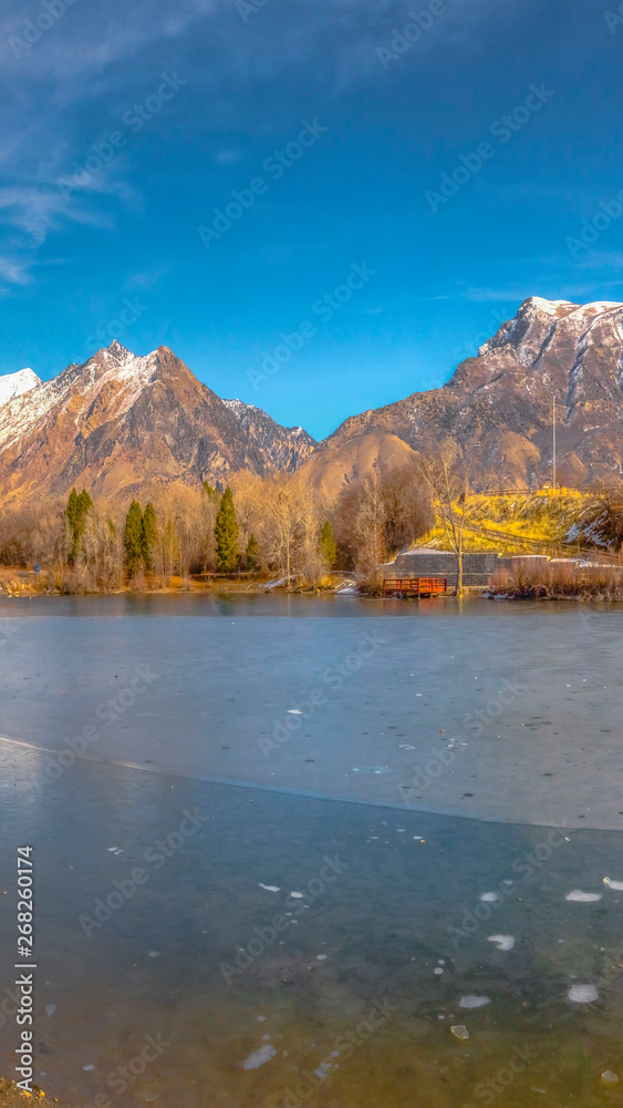 Vertical Scenic panorama of a lake against snow capped mountain and blue sky in winter