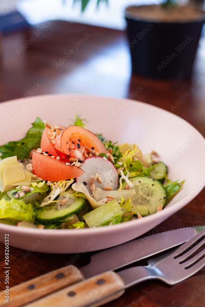Vegan summer salad with fresh tomatoes, crunchy cucumbers and greens on a dark wooden table with cutlery on it Vegan summer salad with fresh tomatoes, crunchy cucumbers and greens on a dark wooden table with cutlery on it