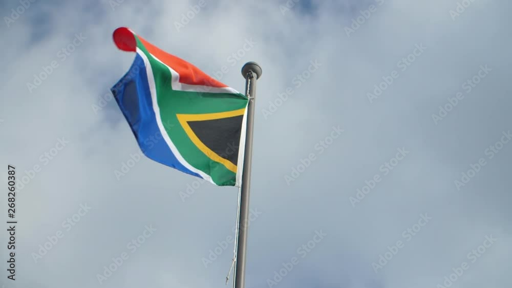 South African flag waving in the wind against cloudy blue sky backdrop on sunny day South African flag waving in the wind against cloudy blue sky backdrop on sunny day