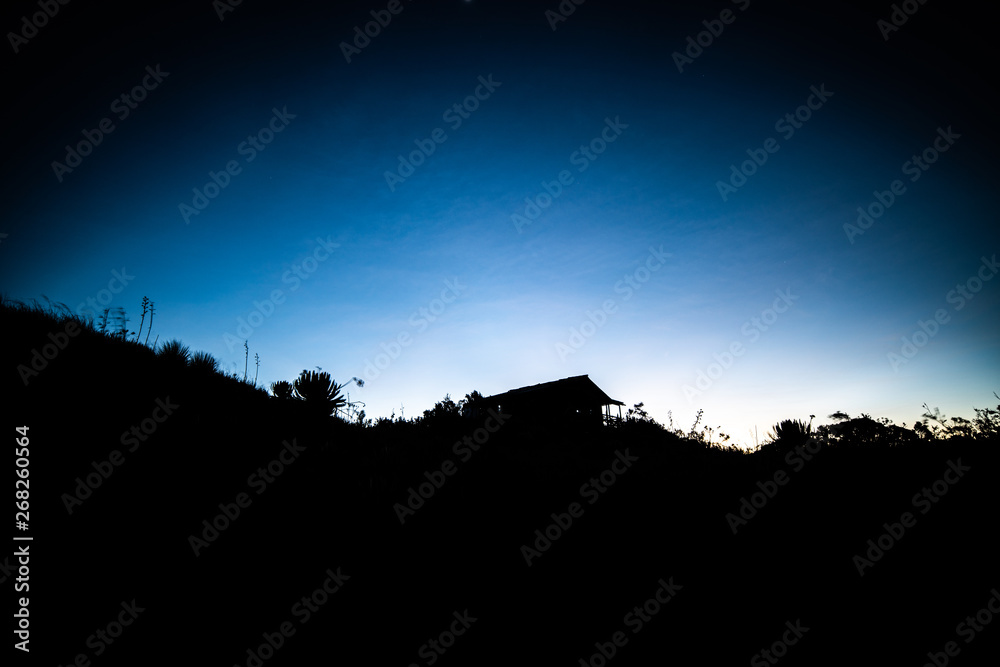 A blue sky during sunrise before the sun rises and the silhouette of a cabin