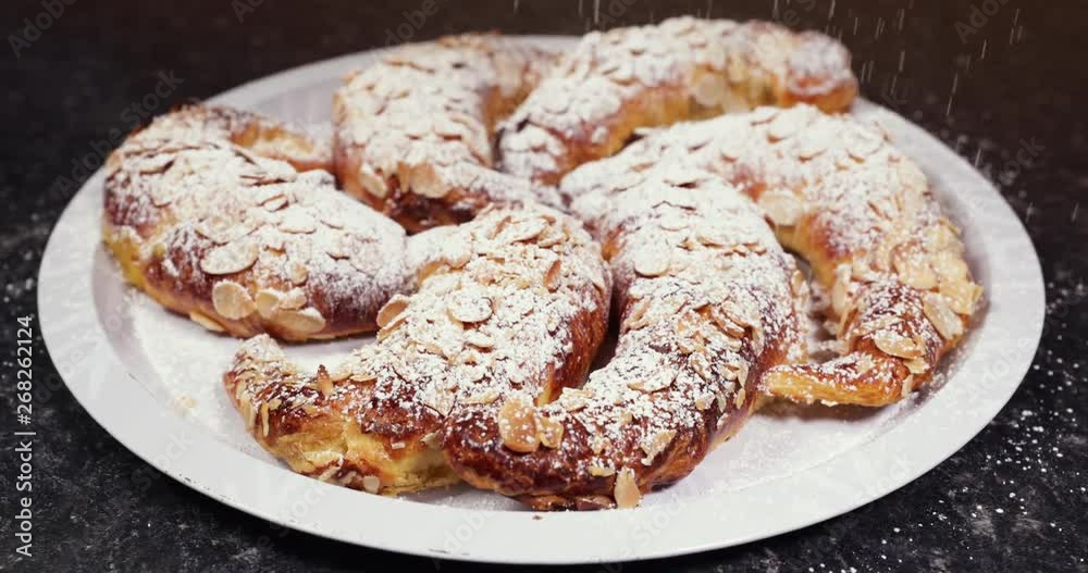 Zooming out SPEED UP shot of beautiful delicious almond croissants ready in a metal tray being powdered with refined sugar- 4K shot at 60pfs Zooming out SPEED UP shot of beautiful delicious almond croissants ready in a metal tray being powdered with refined sugar- 4K shot at 60pfs