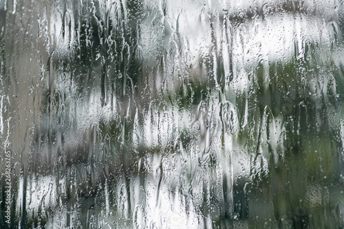 Pouring rain covering the window during a storm; blurred tree shape visible in the background; abstract background