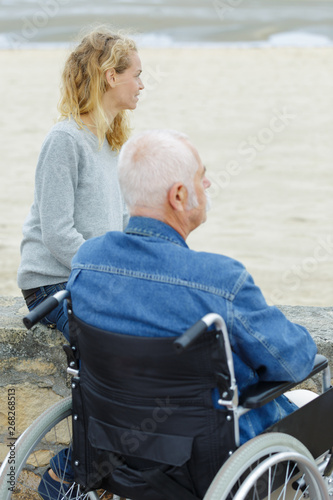 elderly man in wheelchair with his daughter on sea coast