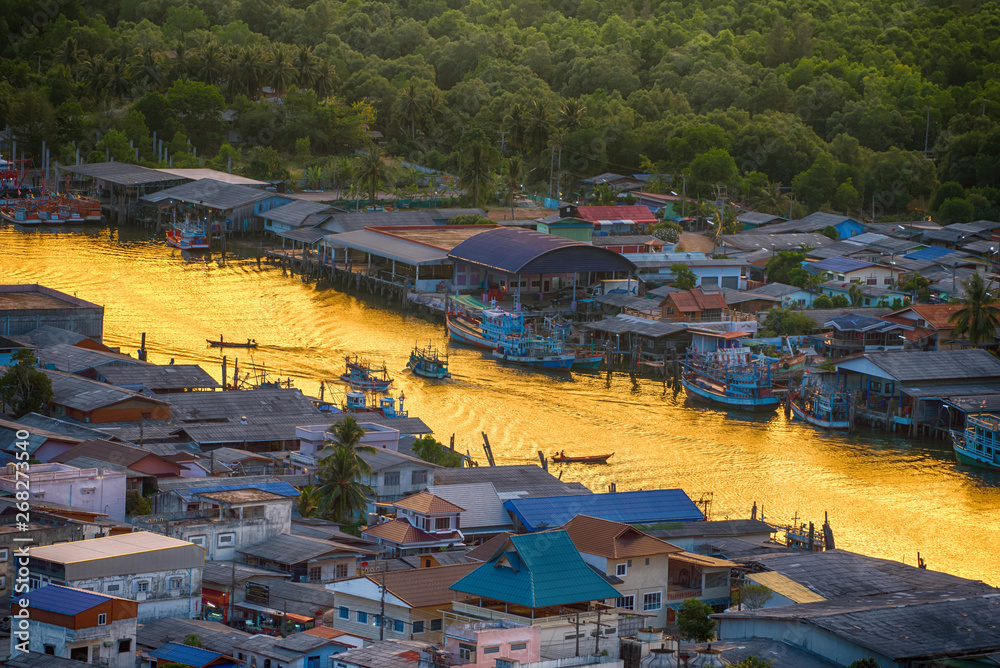 Obraz premium Lifestyle of people in the riverside village during the sunset, The ship is sailing on the river and golden light of the sky at sunset reflected on the water surface. Ban Pak Nam, Chumphon, Thailand.