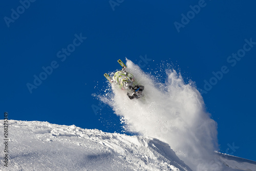 snowmobile jump straight up. the guy is flying and jumping on a snowmobile on a background of blue sky leaving a trail of splashes of white snow. bright snowmobile and suit. No brands. extra quality