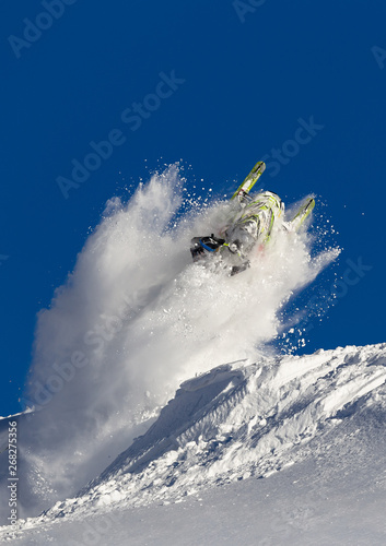 snowmobile jump straight up. the guy is flying and jumping on a snowmobile on a background of blue sky leaving a trail of splashes of white snow. bright snowmobile and suit. No brands. extra quality
