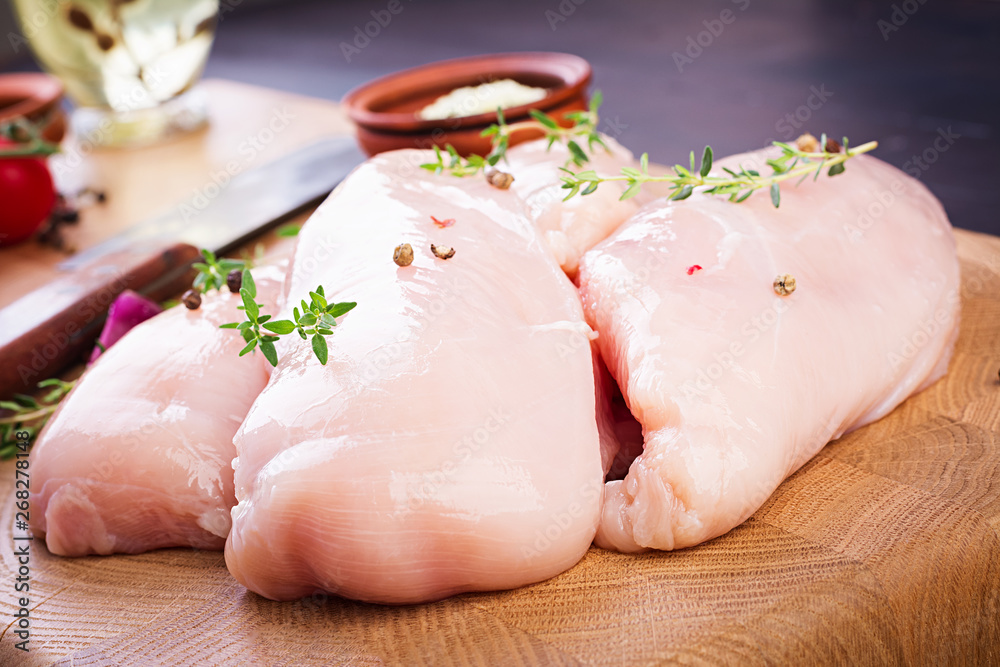 Raw chicken breast fillets on wooden cutting board with herbs and spices. Raw chicken breast fillets on wooden cutting board with herbs and spices.